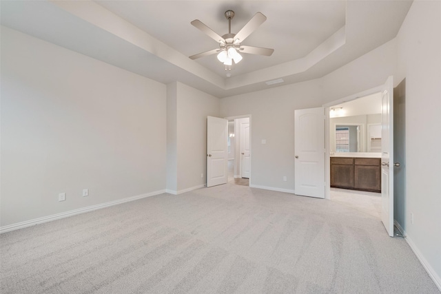 unfurnished bedroom with baseboards, a raised ceiling, a ceiling fan, connected bathroom, and light colored carpet