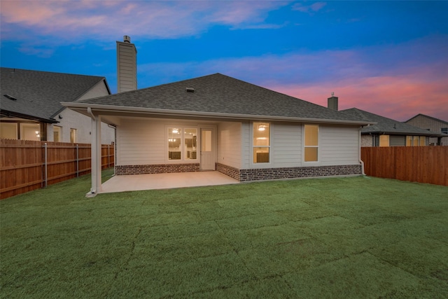 back of property at dusk with brick siding, a chimney, a lawn, a patio area, and a fenced backyard