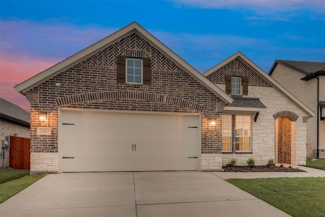 french country style house featuring a garage, concrete driveway, stone siding, roof with shingles, and brick siding