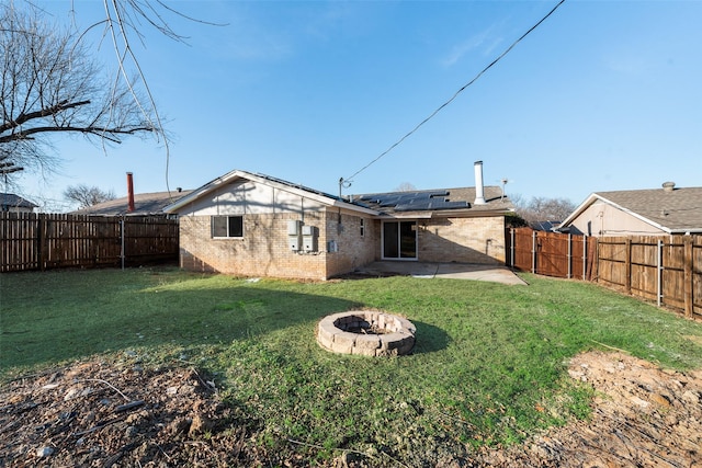 rear view of property with solar panels, a yard, a fire pit, and a patio area