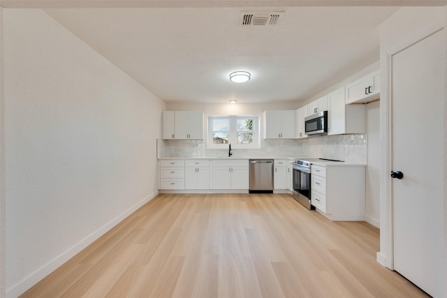 kitchen with white cabinets, sink, appliances with stainless steel finishes, tasteful backsplash, and light hardwood / wood-style floors