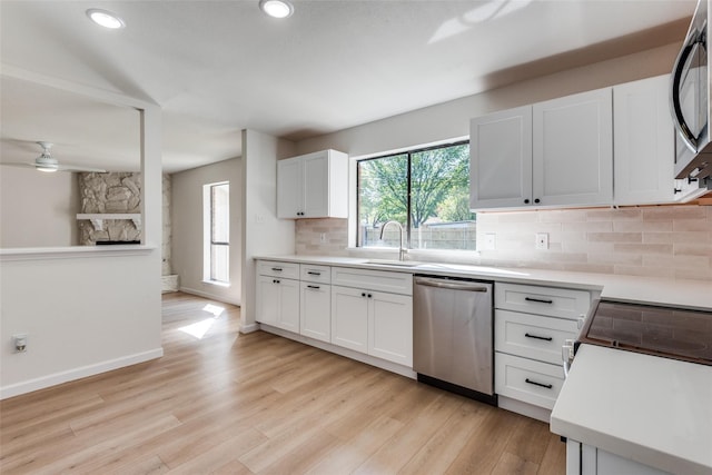 kitchen with a stone fireplace, sink, tasteful backsplash, white cabinetry, and stainless steel appliances