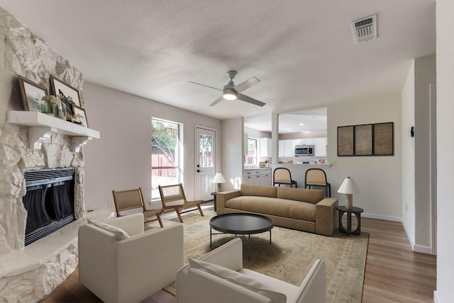 living room featuring a fireplace, light hardwood / wood-style floors, and ceiling fan