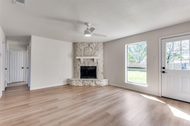 unfurnished living room featuring light wood-type flooring, a stone fireplace, and ceiling fan