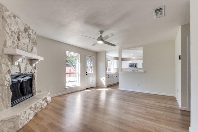 unfurnished living room with ceiling fan, light hardwood / wood-style floors, and a stone fireplace