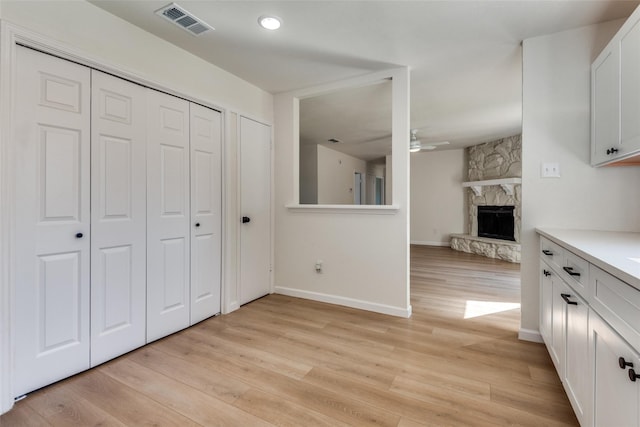 interior space with ceiling fan, a fireplace, white cabinets, and light wood-type flooring