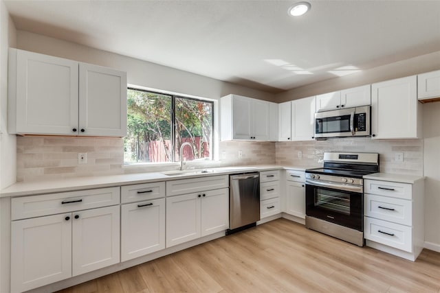 kitchen with light wood-type flooring, tasteful backsplash, stainless steel appliances, sink, and white cabinets