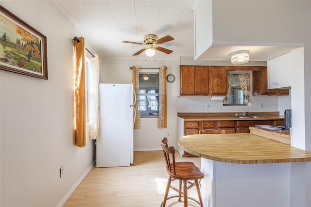 kitchen with a breakfast bar, a peninsula, freestanding refrigerator, brown cabinets, and ceiling fan