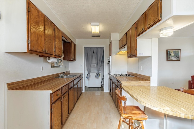 kitchen featuring light wood-style flooring, crown molding, under cabinet range hood, and visible vents