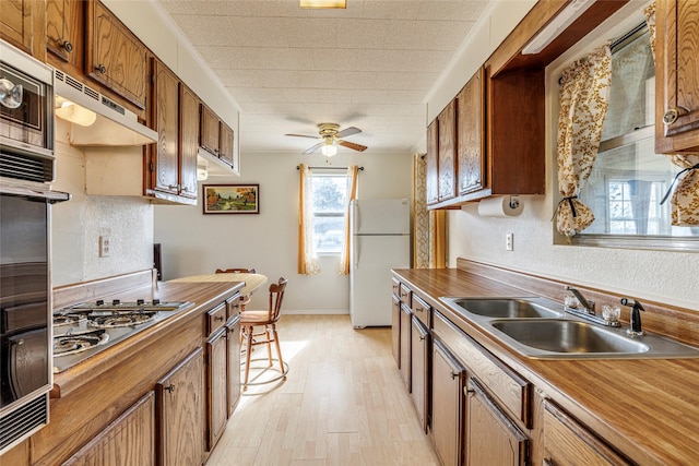 kitchen with a sink, ceiling fan, appliances with stainless steel finishes, light wood-style floors, and brown cabinetry