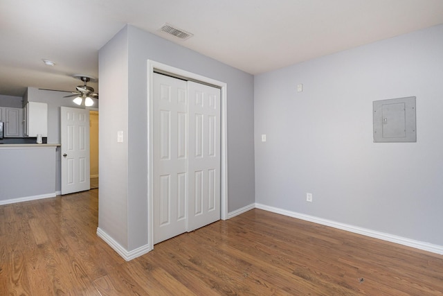 unfurnished bedroom featuring hardwood / wood-style floors, ceiling fan, electric panel, and a closet