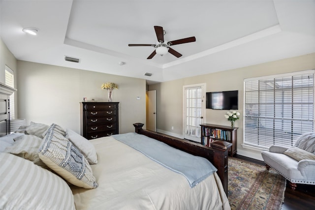 bedroom featuring a raised ceiling, dark wood-type flooring, and ceiling fan