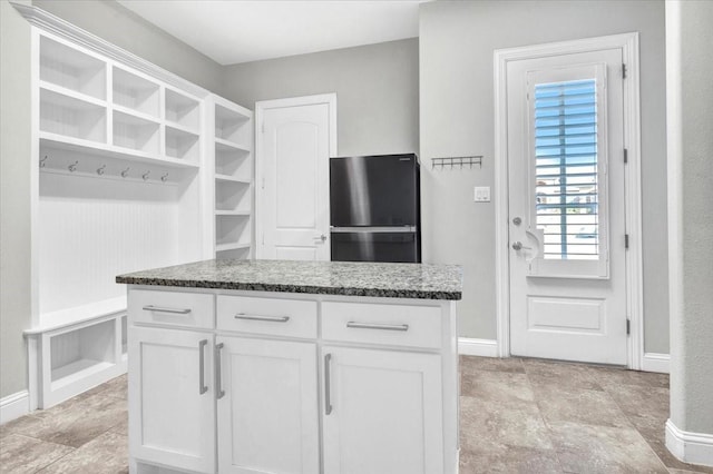 kitchen featuring a kitchen island, dark stone countertops, white cabinetry, and fridge