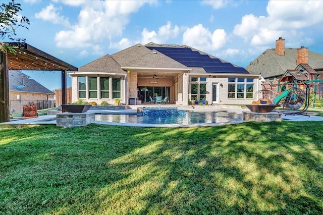 rear view of property featuring a playground, solar panels, ceiling fan, and a yard