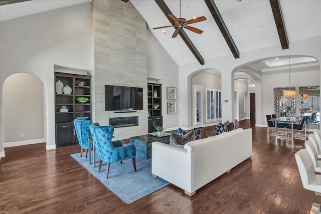 living room featuring built in shelves, a tile fireplace, beamed ceiling, high vaulted ceiling, and ceiling fan with notable chandelier