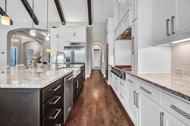 kitchen with appliances with stainless steel finishes, white cabinets, a kitchen island with sink, beamed ceiling, and hanging light fixtures