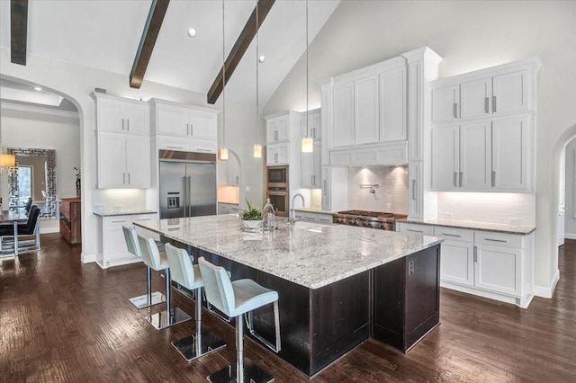 kitchen with backsplash, a large island with sink, built in appliances, white cabinets, and a breakfast bar area