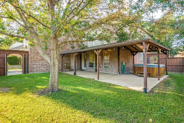 rear view of property with ceiling fan, a patio area, a yard, and a hot tub