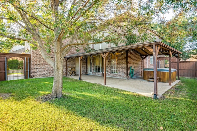 back of house featuring a hot tub, a patio area, and a lawn