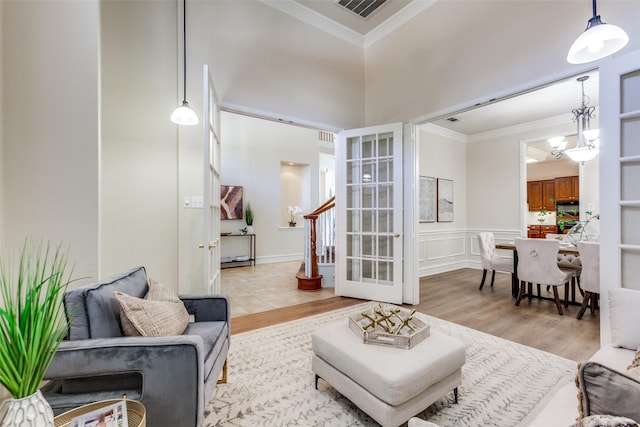 living room featuring a high ceiling, ornamental molding, a chandelier, and light hardwood / wood-style floors