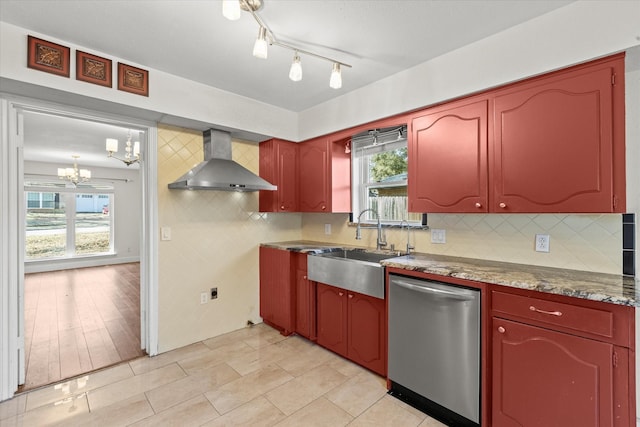 kitchen featuring wall chimney exhaust hood, sink, an inviting chandelier, stainless steel dishwasher, and a healthy amount of sunlight