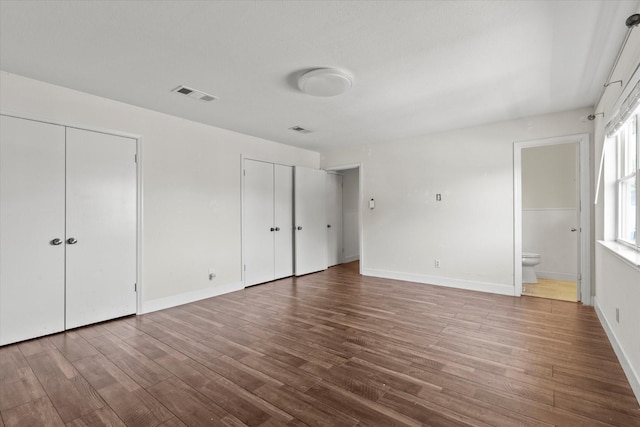 unfurnished bedroom featuring hardwood / wood-style flooring, ensuite bath, and two closets