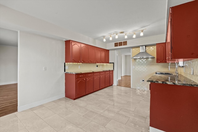 kitchen with tasteful backsplash, wall chimney exhaust hood, sink, and dark stone counters