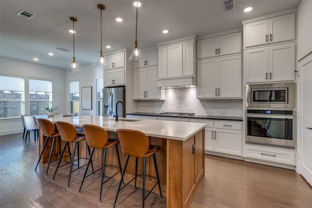 kitchen with pendant lighting, appliances with stainless steel finishes, a kitchen island with sink, and white cabinets