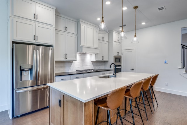 kitchen with white cabinetry, pendant lighting, stainless steel appliances, and an island with sink