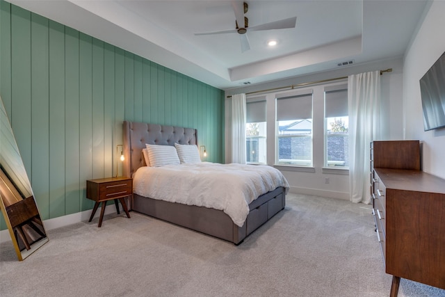 bedroom featuring light carpet, wood walls, ceiling fan, and a tray ceiling