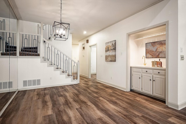 unfurnished living room with a notable chandelier, dark hardwood / wood-style flooring, sink, and crown molding