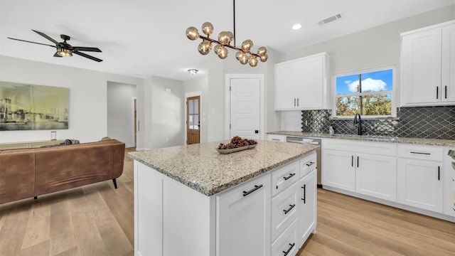 kitchen with white cabinets, decorative light fixtures, a kitchen island, and sink