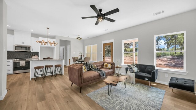 living room with ceiling fan with notable chandelier and light hardwood / wood-style flooring