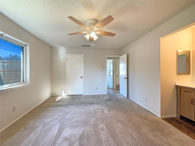 unfurnished bedroom with connected bathroom, ceiling fan, light carpet, and a textured ceiling