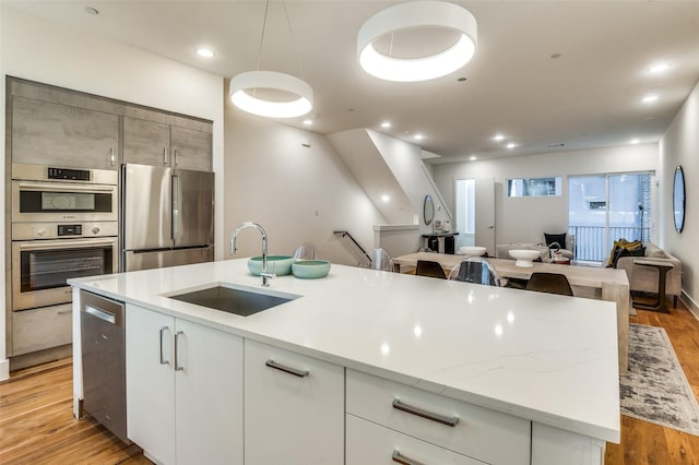 kitchen featuring sink, appliances with stainless steel finishes, a kitchen island with sink, white cabinets, and light wood-type flooring