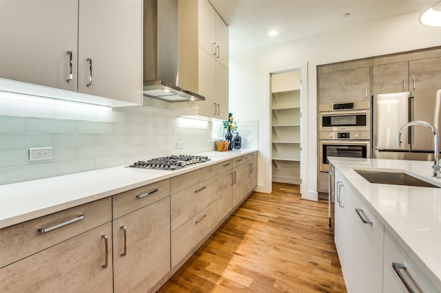 kitchen with decorative backsplash, appliances with stainless steel finishes, sink, wall chimney range hood, and light hardwood / wood-style flooring