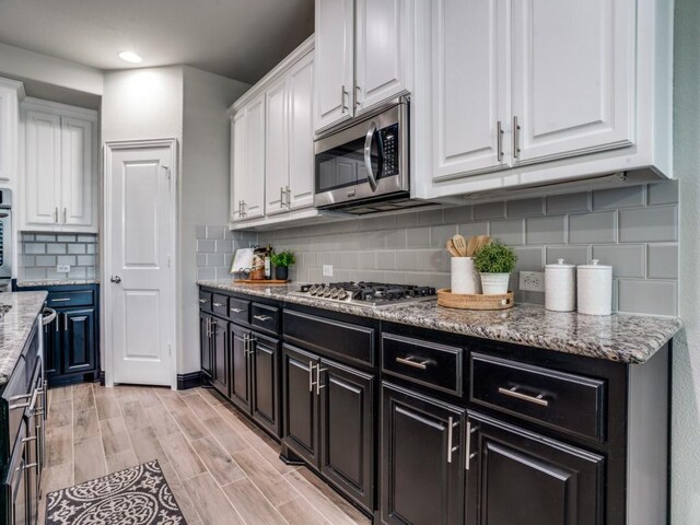 kitchen with white cabinets, appliances with stainless steel finishes, decorative backsplash, and light stone countertops