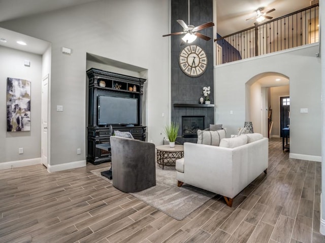 living room with a towering ceiling, ceiling fan, and a tiled fireplace