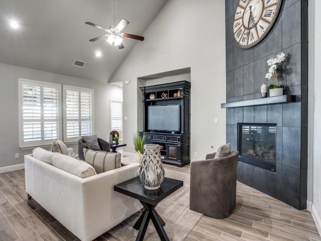 living room featuring high vaulted ceiling, ceiling fan, and a tile fireplace