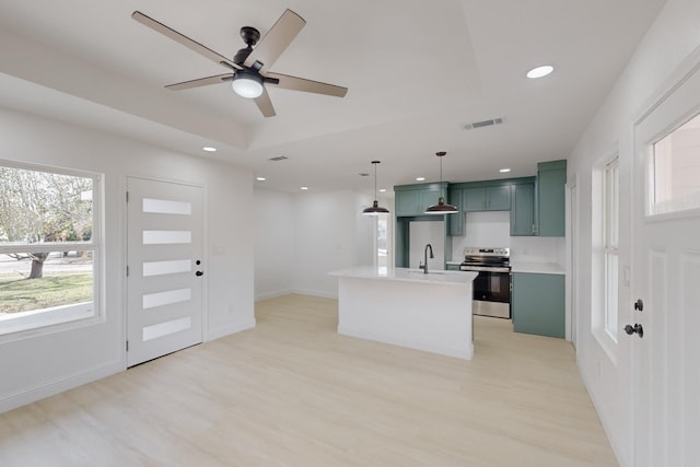 kitchen featuring stainless steel electric stove, an island with sink, hanging light fixtures, a raised ceiling, and light hardwood / wood-style flooring