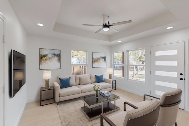 living room with a tray ceiling, ceiling fan, and light hardwood / wood-style floors