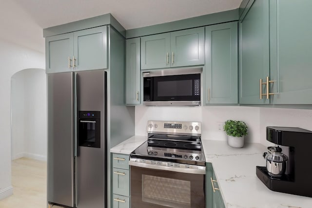 kitchen featuring green cabinets, light stone countertops, and appliances with stainless steel finishes