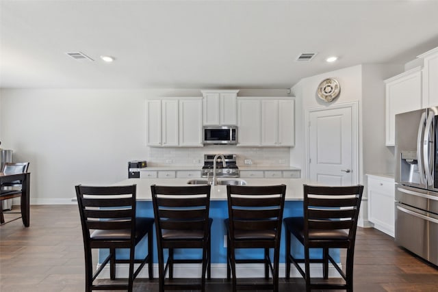 kitchen featuring white cabinetry, a kitchen island with sink, decorative backsplash, a breakfast bar, and appliances with stainless steel finishes