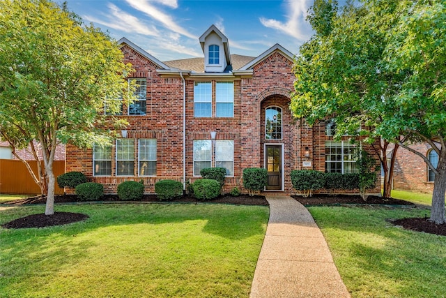 traditional-style home featuring roof with shingles, brick siding, a front lawn, and fence