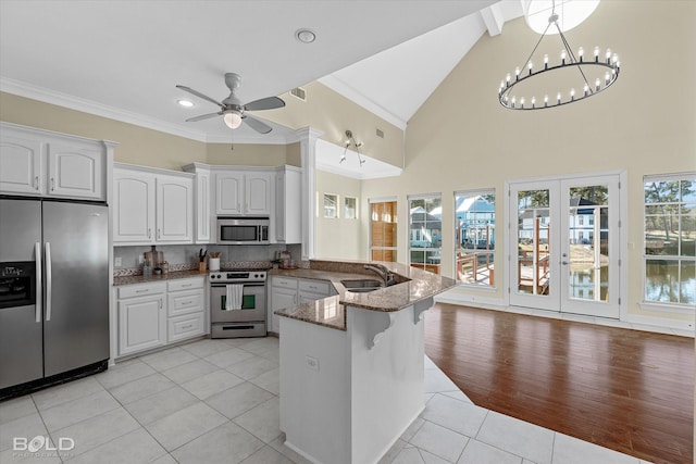 kitchen with kitchen peninsula, light tile patterned floors, appliances with stainless steel finishes, white cabinets, and dark stone counters