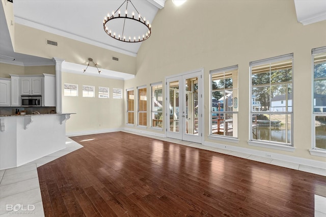 unfurnished living room with a high ceiling, light hardwood / wood-style flooring, crown molding, and an inviting chandelier