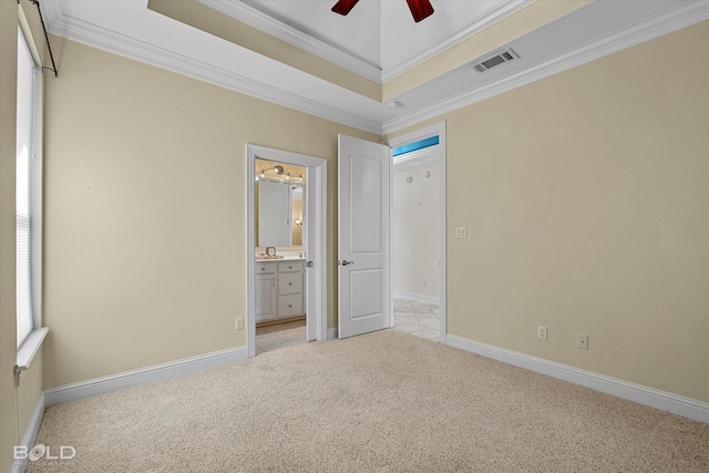 unfurnished bedroom with light carpet, ceiling fan, a tray ceiling, ensuite bath, and ornamental molding