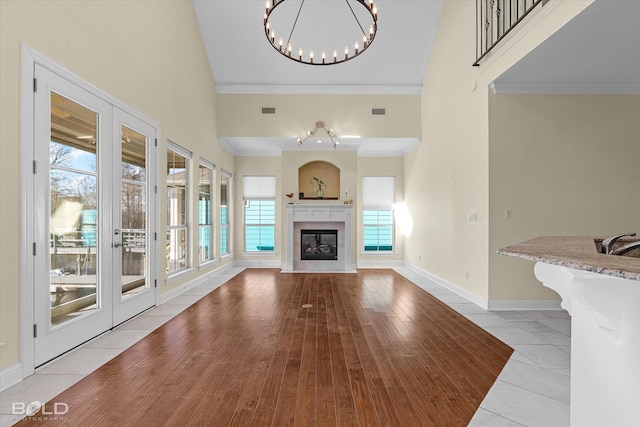 unfurnished living room with light tile patterned floors, a notable chandelier, french doors, crown molding, and sink