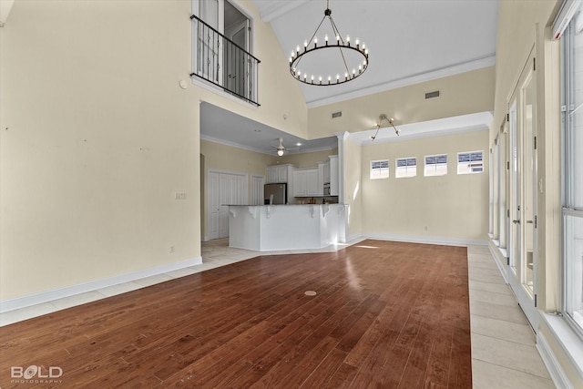 unfurnished living room with ceiling fan with notable chandelier, a high ceiling, and light hardwood / wood-style floors