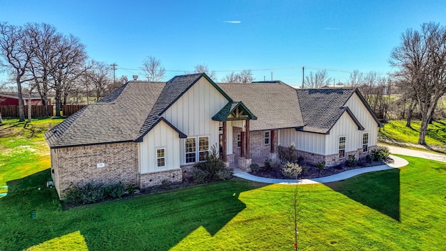 modern inspired farmhouse featuring a front lawn, stone siding, board and batten siding, a shingled roof, and brick siding